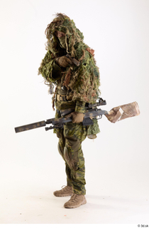 Andrew Elliott in Ghillie Pose with Gun holding gun standing…